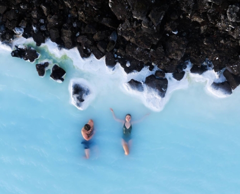 Vista aérea de dos personas en aguas termales de la Laguna Azul rodeadas de rocas volcánicas en Islandia