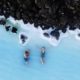 Vista aérea de dos personas en aguas termales de la Laguna Azul rodeadas de rocas volcánicas en Islandia