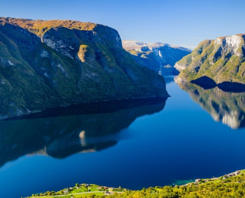 Fiordo rodeado de montañas reflejadas en el agua con una embarcación navegando en Noruega