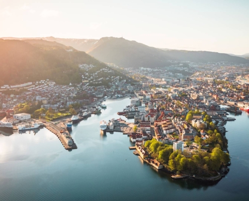 Vista aérea de Bergen junto al fiordo con puerto, colinas verdes y viviendas costeras