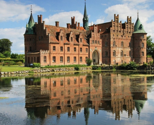 Castillo de Egeskov reflejado en el agua con fachada renacentista y jardines en Dinamarca