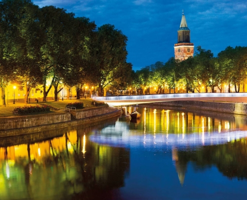 Costa histórica de Turku iluminada al anochecer con edificios reflejados en el río Aura