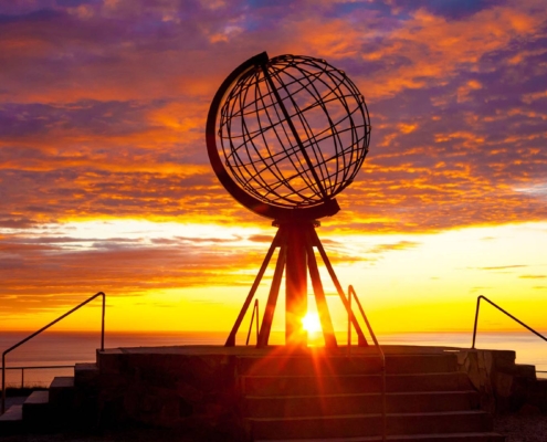 Globo metálico de Cabo Norte iluminado por el sol de medianoche frente al océano Ártico