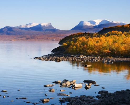 Paisaje lacustre en Abisko con costa rocosa, montañas suaves y agua en calma en Laponia sueca
