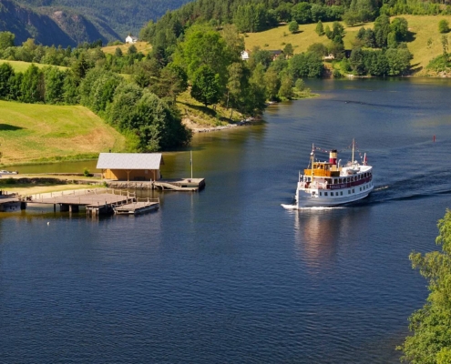 Barco navegando por el canal de Telemark entre colinas verdes y orillas arboladas, Noruega