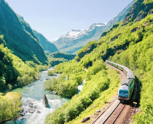 Tren recorriendo el valle del Flåm entre montañas verdes y el rio, Noruega