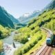 Tren recorriendo el valle del Flåm entre montañas verdes y el rio, Noruega