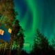 Cabaña suspendida entre árboles bajo auroras boreales en entorno forestal de Laponia Sueca