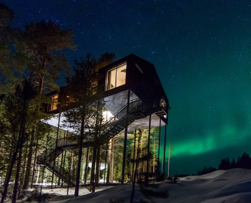 Cabaña del Treehotel iluminada de noche entre árboles nevados en Laponia Sueca