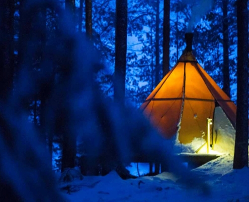 Tienda de glamping iluminada en bosque nevado durante noche invernal en Laponia Sueca