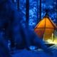 Tienda de glamping iluminada en bosque nevado durante noche invernal en Laponia Sueca