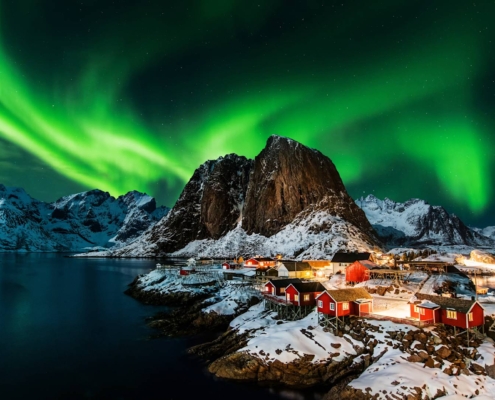 Cabañas de pescadores rojas junto al mar bajo auroras boreales en las islas Lofoten, Noruega
