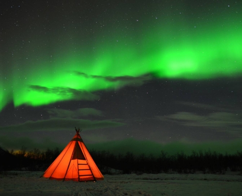 Tienda de campaña iluminada bajo auroras boreales en bosque ártico cerca de Abisko