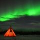 Tienda de campaña iluminada bajo auroras boreales en bosque ártico cerca de Abisko