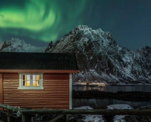 Cabaña de pescadores junto al mar con auroras boreales sobre montañas en las islas Lofoten