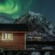 Cabaña de pescadores junto al mar con auroras boreales sobre montañas en las islas Lofoten