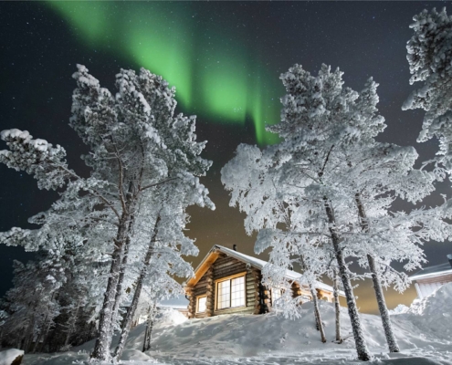 Auroras boreales sobre lago Inari helado junto a cabañas de madera en Laponia