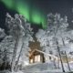 Auroras boreales sobre lago Inari helado junto a cabañas de madera en Laponia