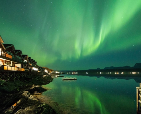 Cabañas iluminadas frente al fiordo de Malangen bajo auroras boreales en Tromsø, Noruega