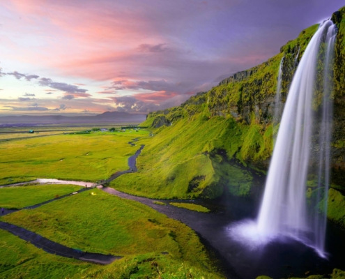 Cascada Seljalandsfoss rodeada de praderas verdes y acantilados volcánicos en Islandia