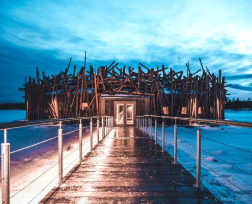 Vista nocturna del hotel Arctic Bath con pasarela iluminada en paisaje invernal