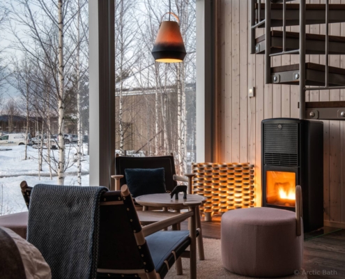 Salón interior de Arctic Bath con chimenea y ambiente acogedor frente al paisaje nevado