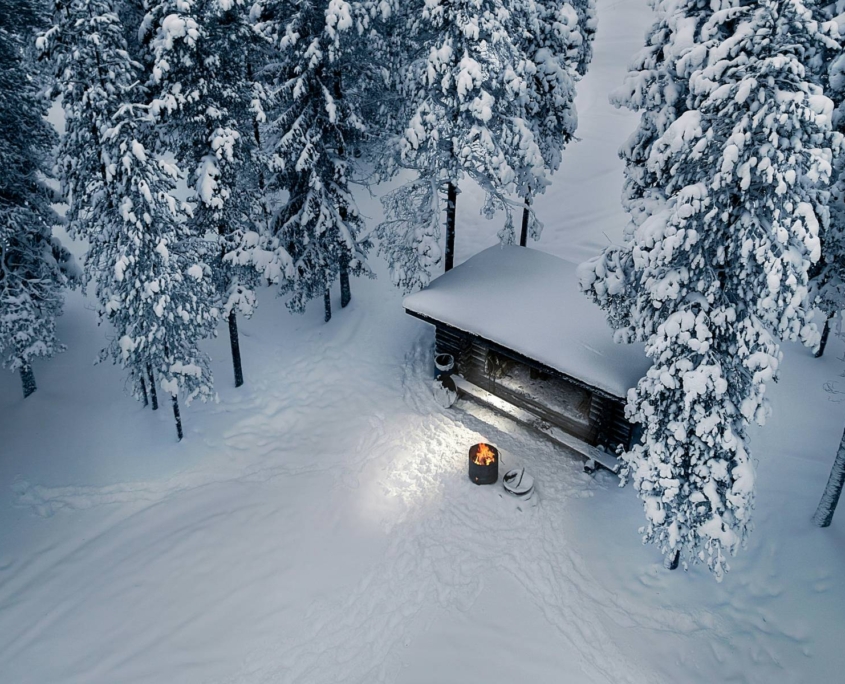 Cabaña iluminada rodeada de nieve al anochecer entre árboles invernales