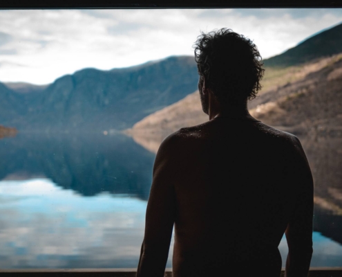 Persona contemplando el fiordo desde sauna flotante rodeada de montañas