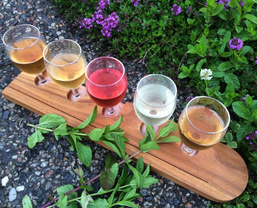 Tabla de madera con vasos de sidra colocados sobre grava y vegetación