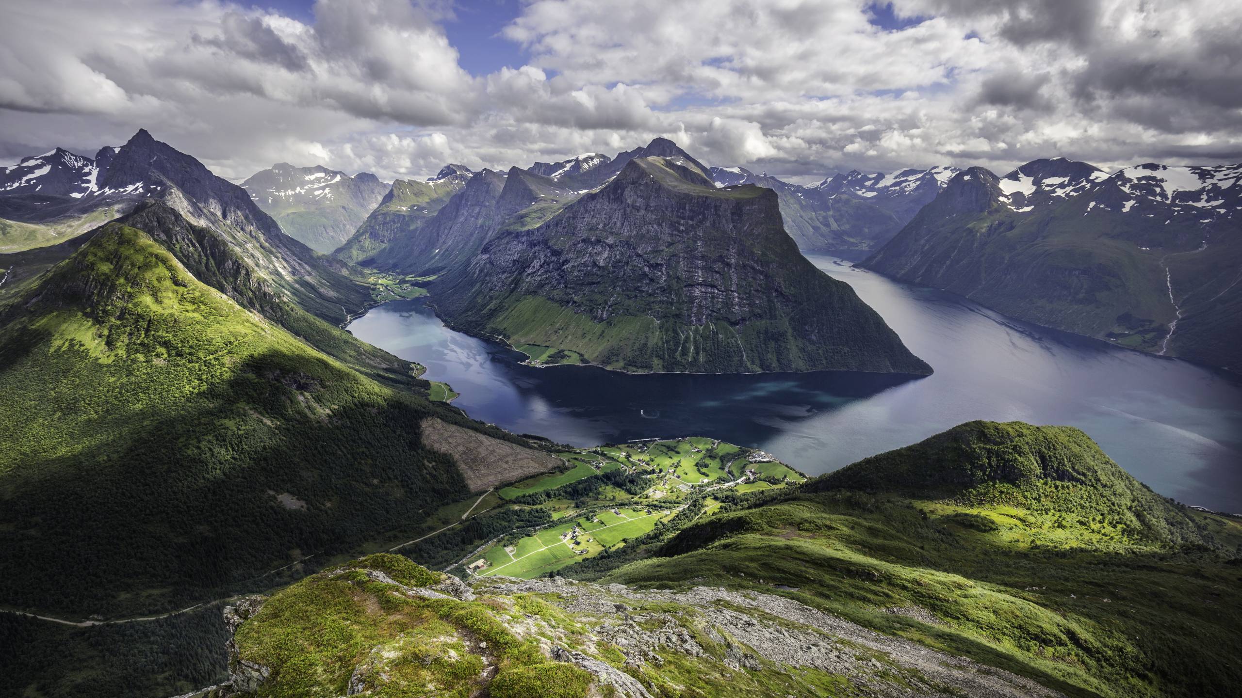 Vista panorámica de fiordo con montañas escarpadas, valle verde y carretera serpenteante en Noruega