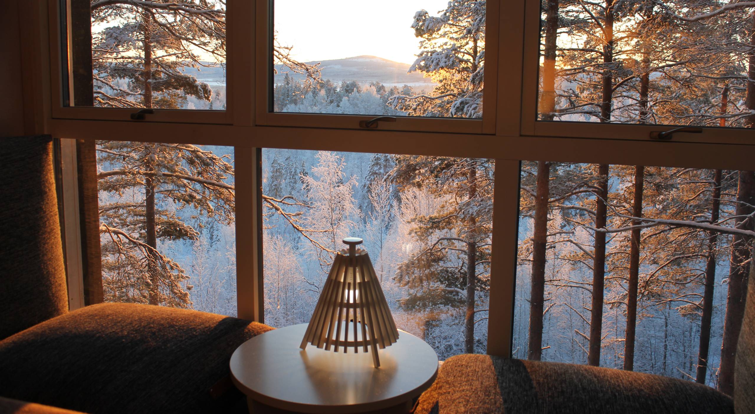 Interior de cabaña de madera con gran ventanal y vistas a bosque boreal nevado