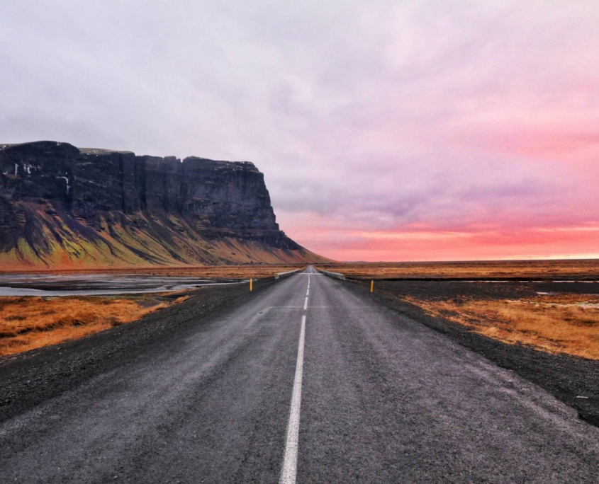 Carretera recta atravesando paisaje abierto de Islandia bajo cielo de atardecer despejado