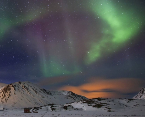 Auroras boreales verdes y violetas sobre montañas nevadas en Alta, Noruega.