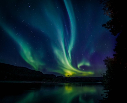Auroras boreales verdes reflejadas en el agua en Alta, Noruega.
