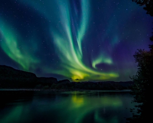 Auroras boreales verdes reflejadas en el agua en Alta, Noruega.