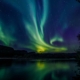 Auroras boreales verdes reflejadas en el agua en Alta, Noruega.