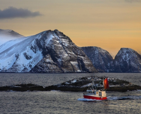 Barco pesquero frente a montañas nevadas en Alta, Noruega.