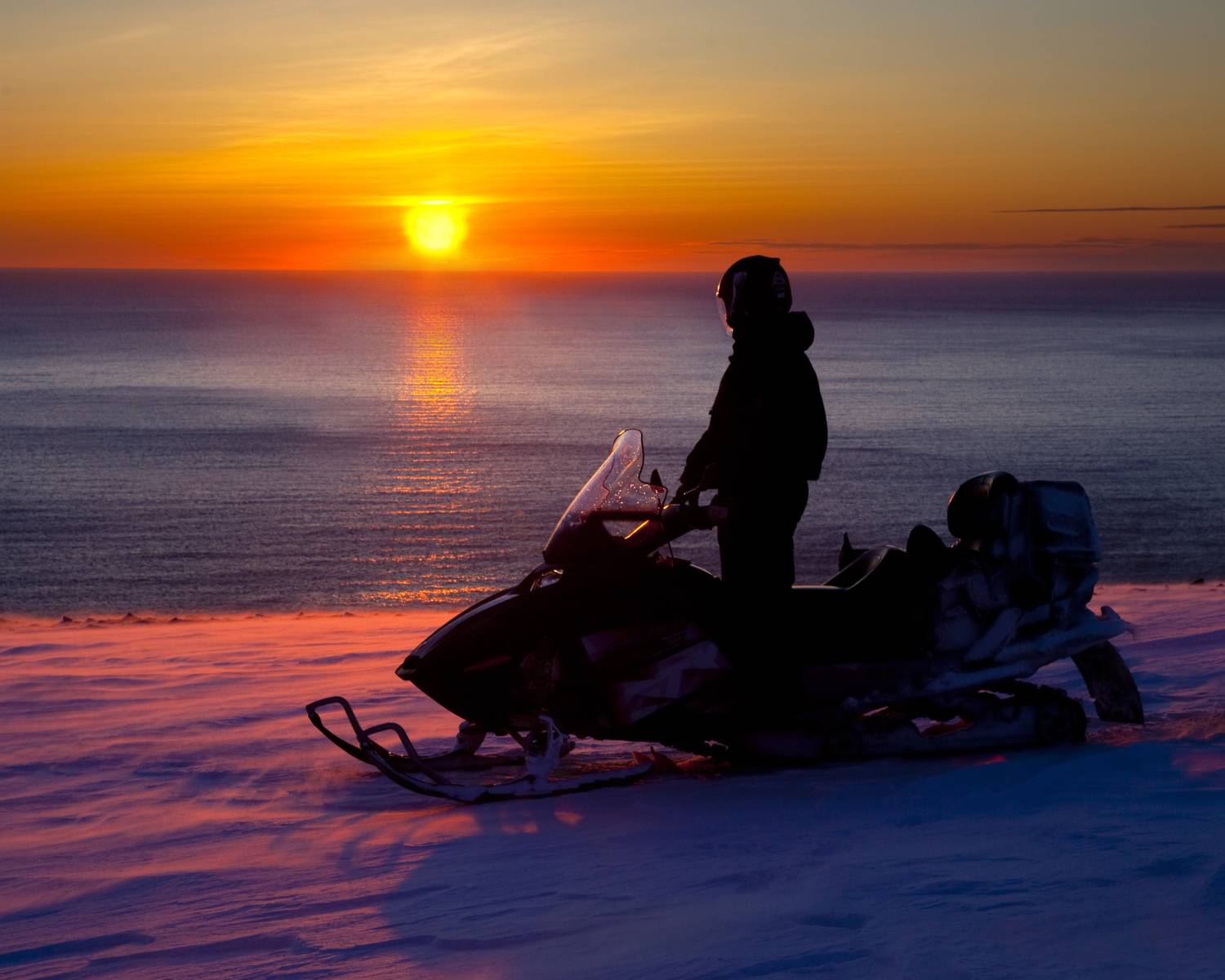Moto de nieve junto al mar bajo un cielo anaranjado en Alta, Noruega.