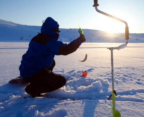 Persona pescando sobre un lago helado junto a una barrena en Alta, Noruega.