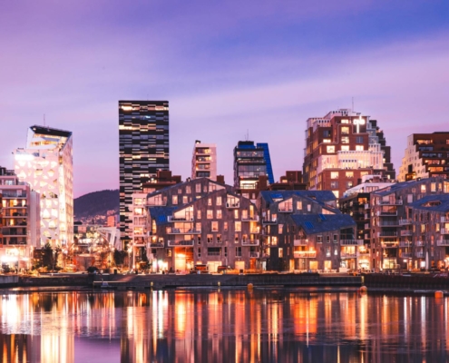 Edificios iluminados del frente marítimo reflejados en el agua en Oslo, Noruega.