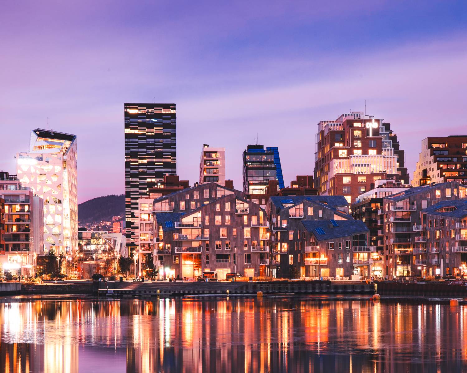Edificios iluminados del frente marítimo reflejados en el agua en Oslo, Noruega.